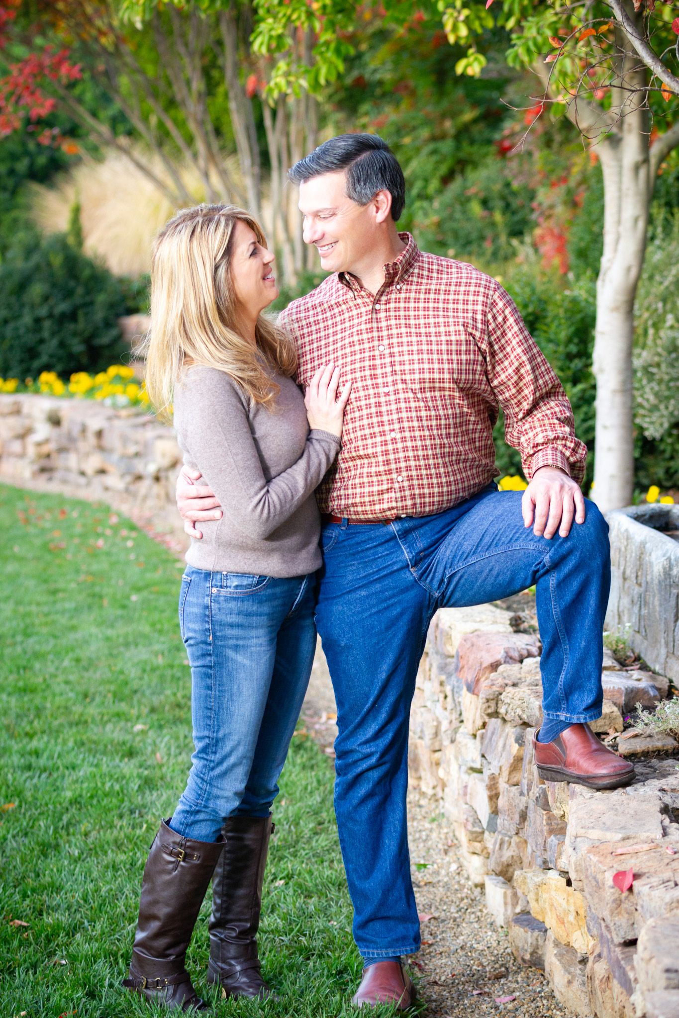 Couple sharing playful moment by stone wall with autumn garden backdrop.