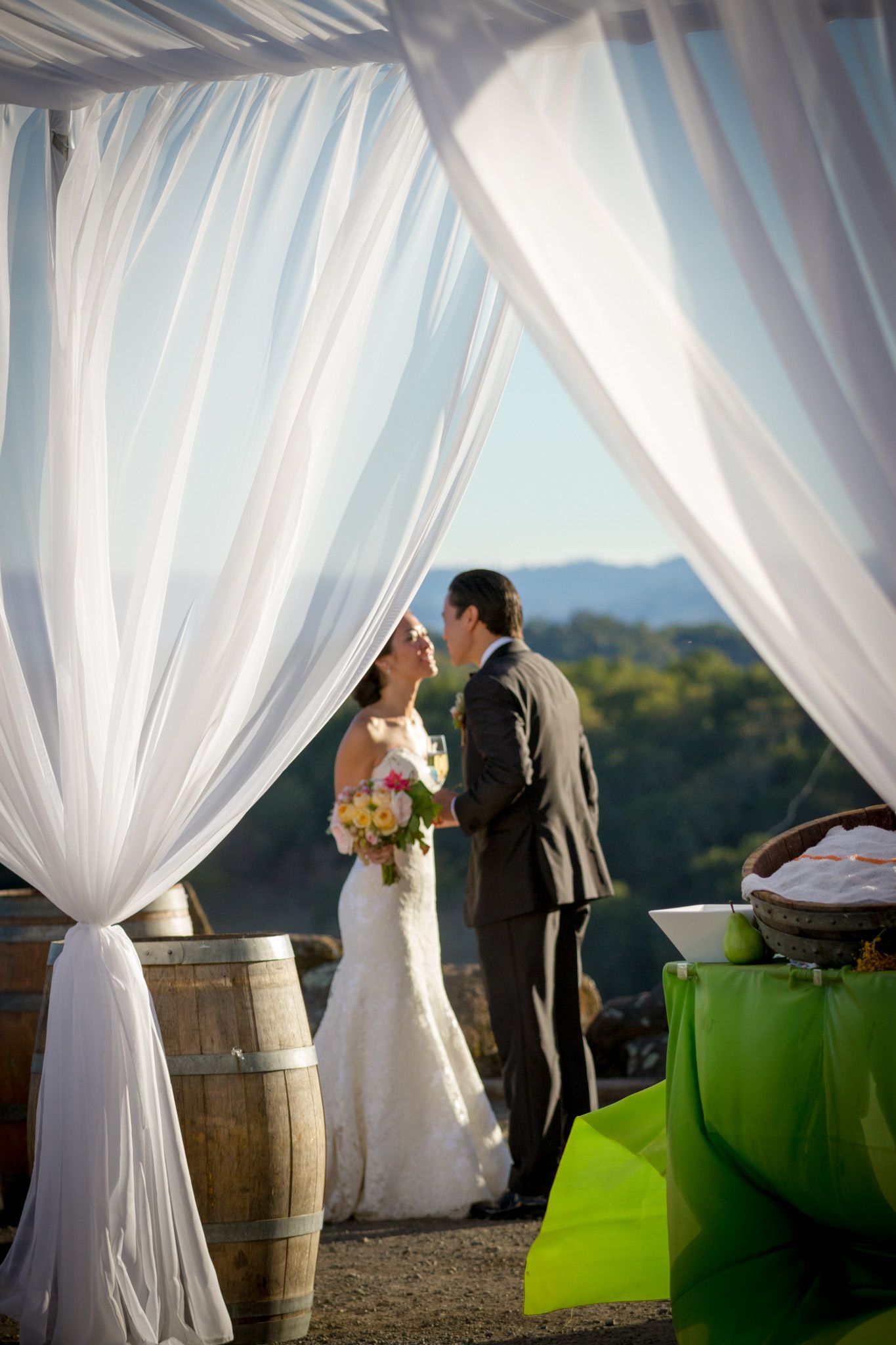 Wedding couple embracing under flowing white fabric canopy with mountain views.