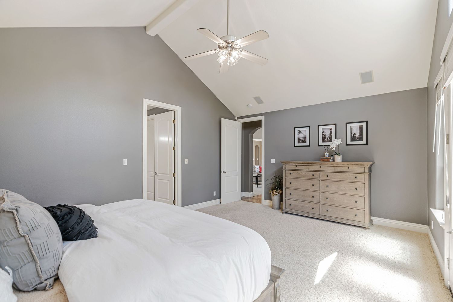 Bright bedroom with vaulted ceiling, ceiling fan, and gray accent wall featuring modern furnishings.
