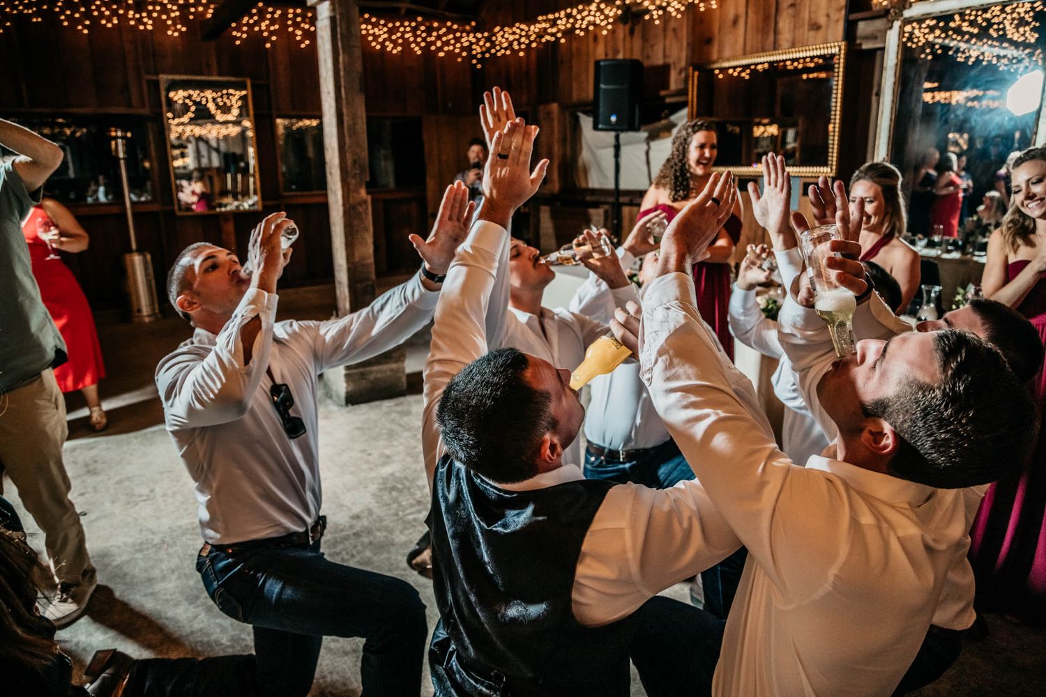 Wedding guests dancing and celebrating with hands in the air under string lights.