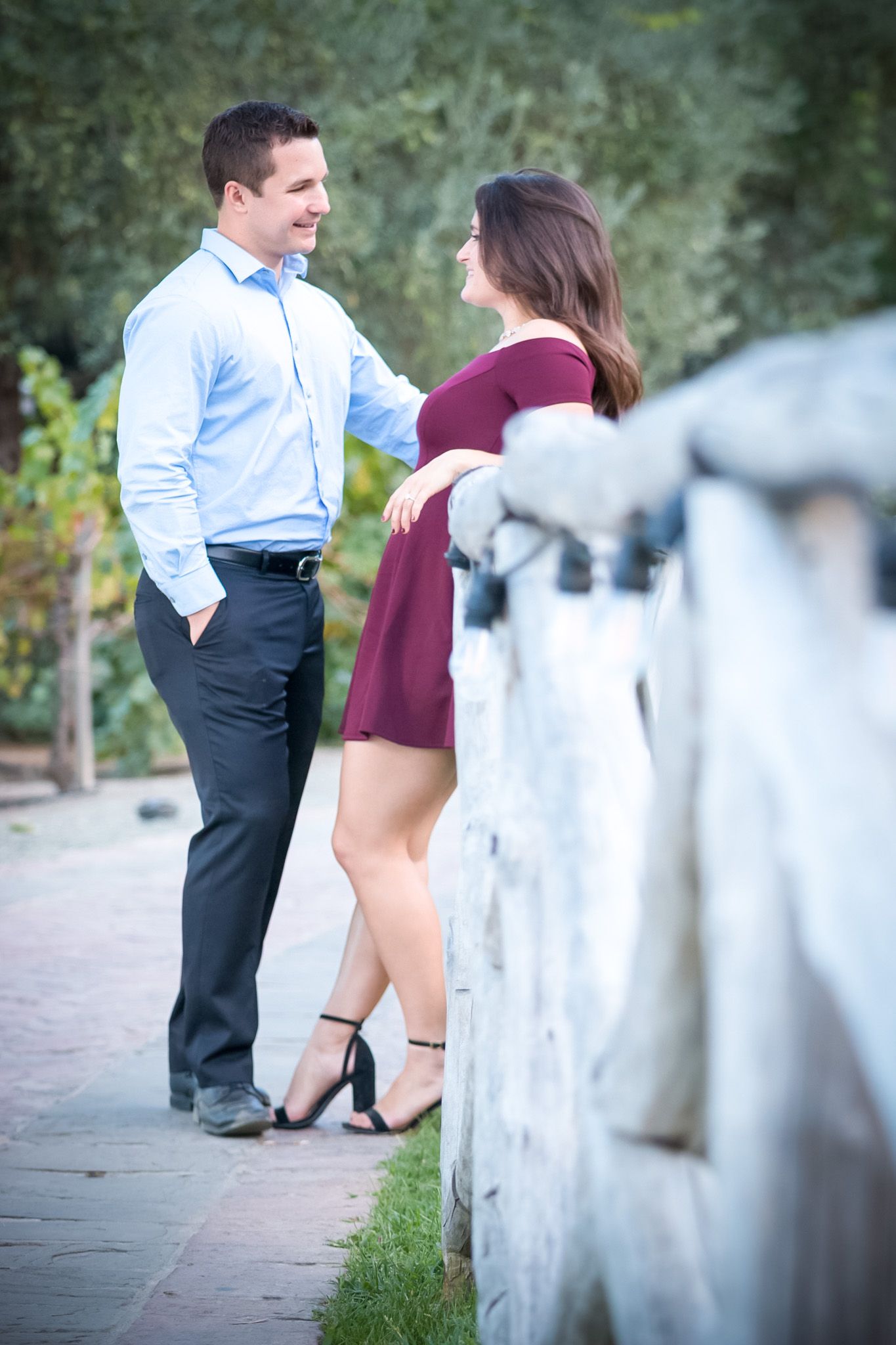 Stylish couple in formal attire poses along white railing pathway.