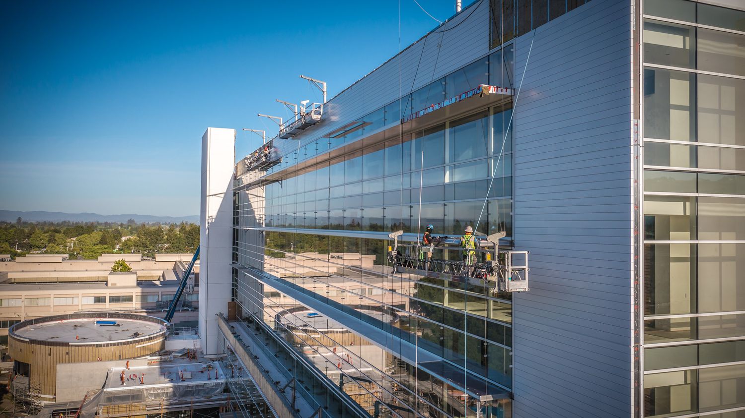 Window washers clean the exterior glass of a modern commercial building against a blue sky.