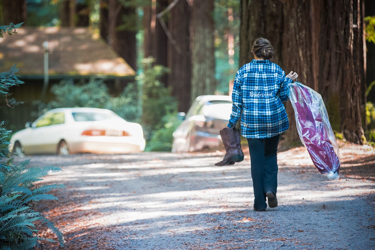 Person carrying purple garment bag while walking on forest path near parked cars.