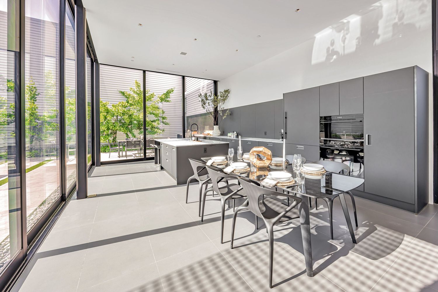 Modern kitchen with gray cabinets, dining area, and floor-to-ceiling windows letting in natural light.