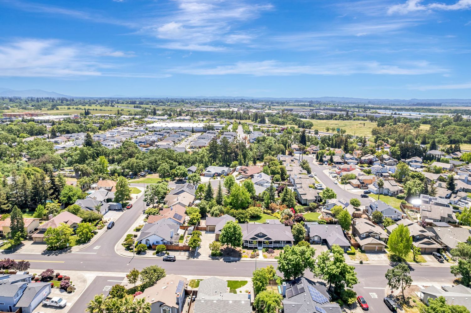 Aerial view of residential neighborhood with suburban homes and tree-lined streets on a sunny day.