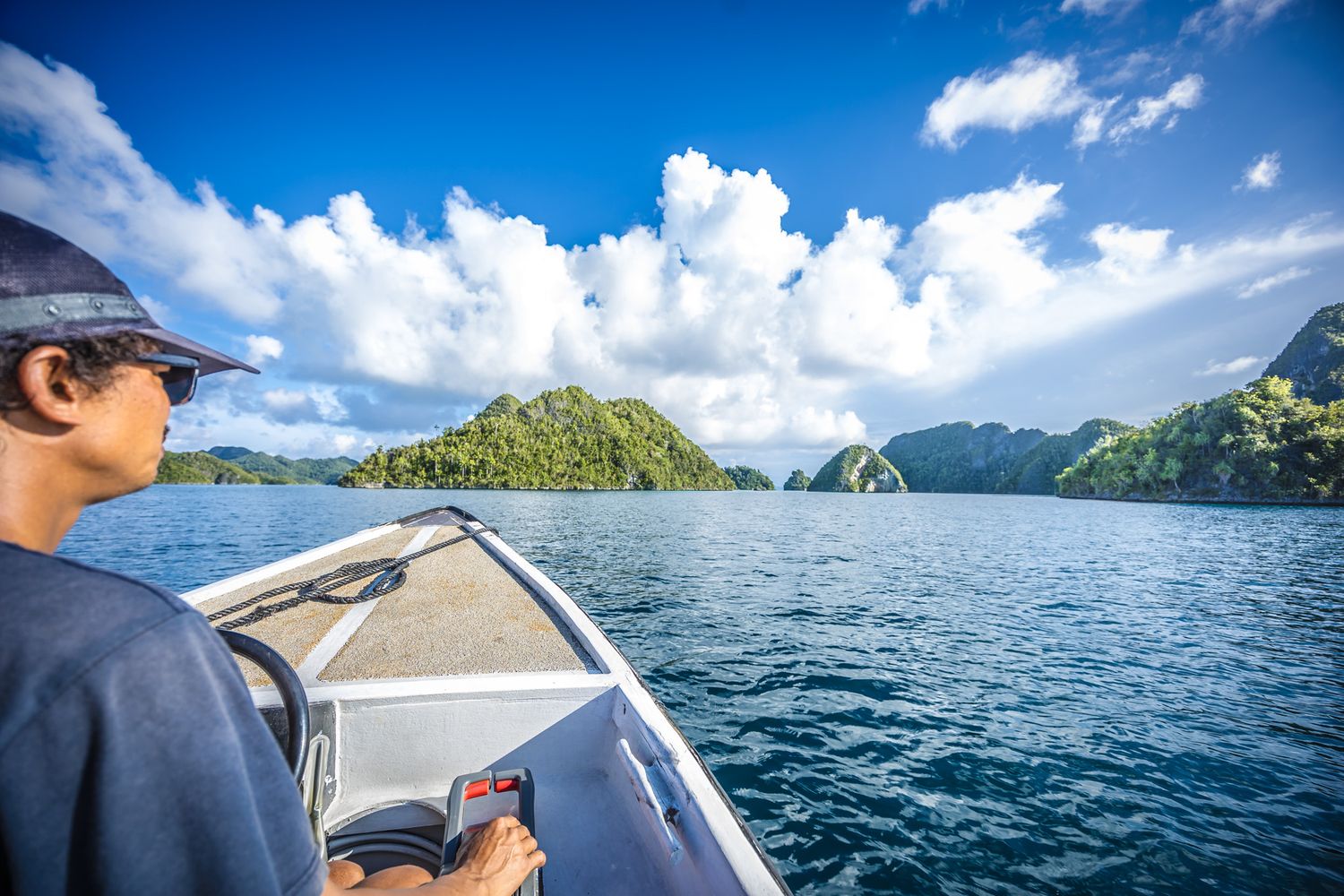 Person steering motorboat through pristine island waters under bright blue skies.