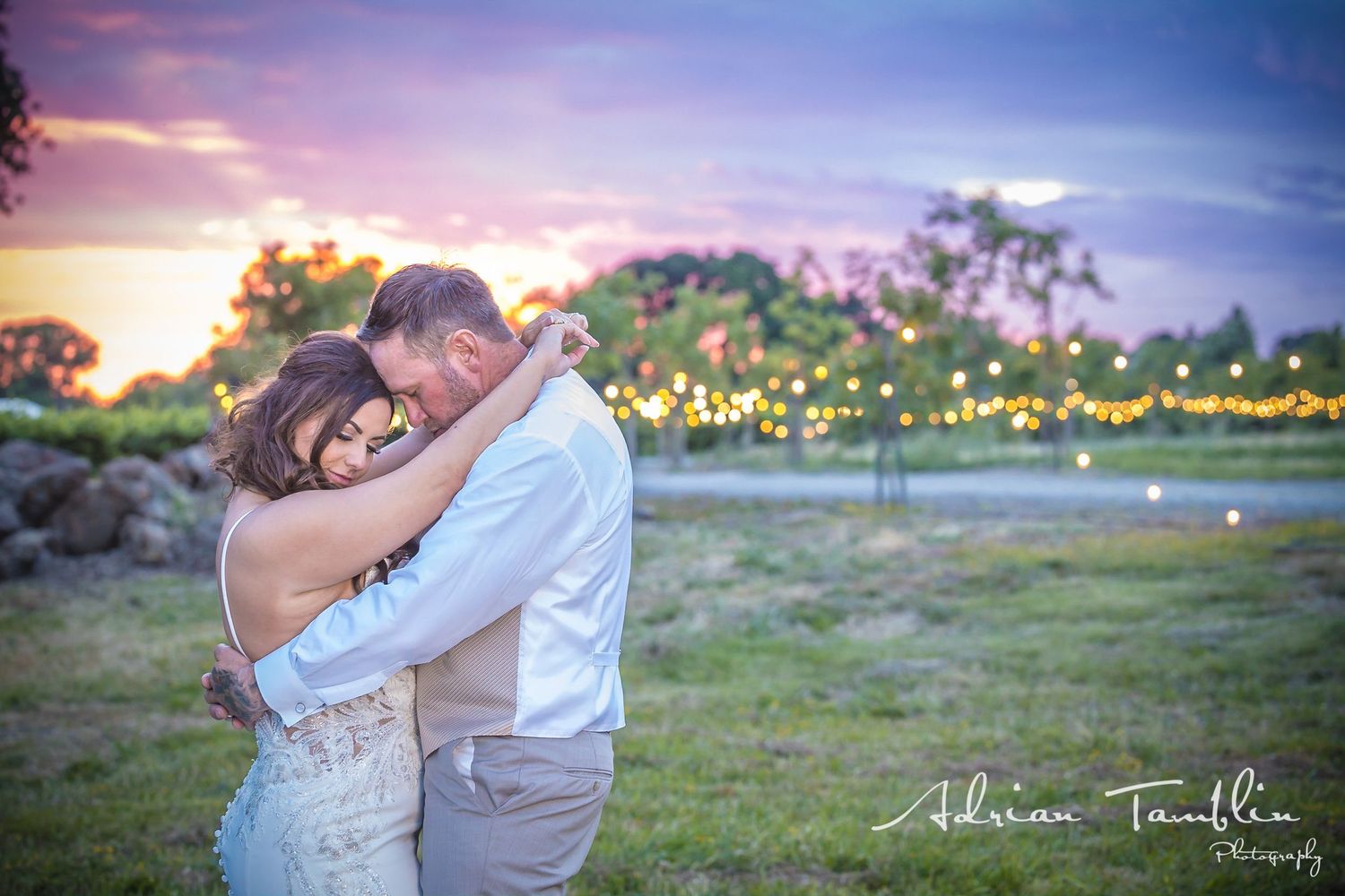 A couple embraces during sunset with string lights glowing in the background.