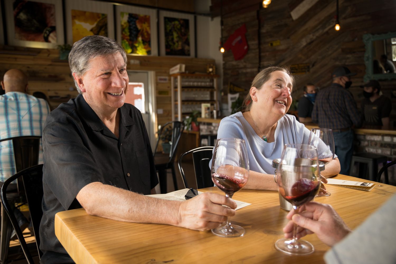 Two patrons sharing drinks and laughter at a wooden table in a casual bar setting.