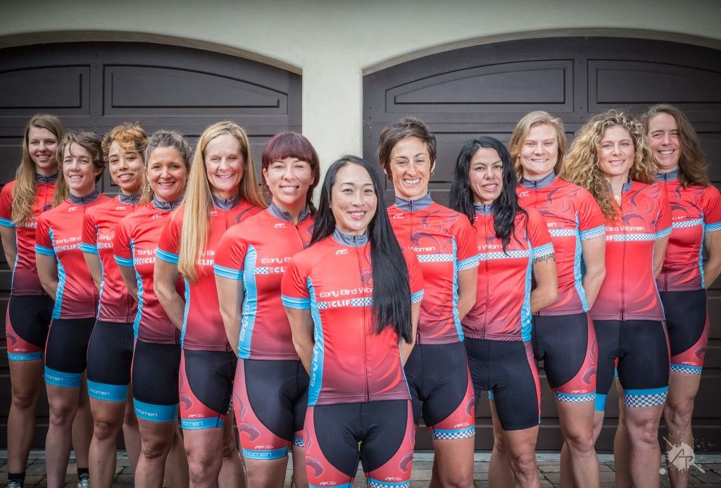 Women's cycling team in matching red jerseys posing together for a group photo.
