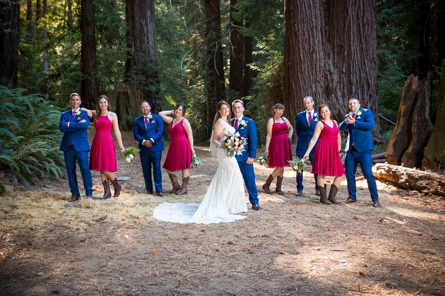 Wedding party in red and blue attire poses playfully on forest path during photo session.