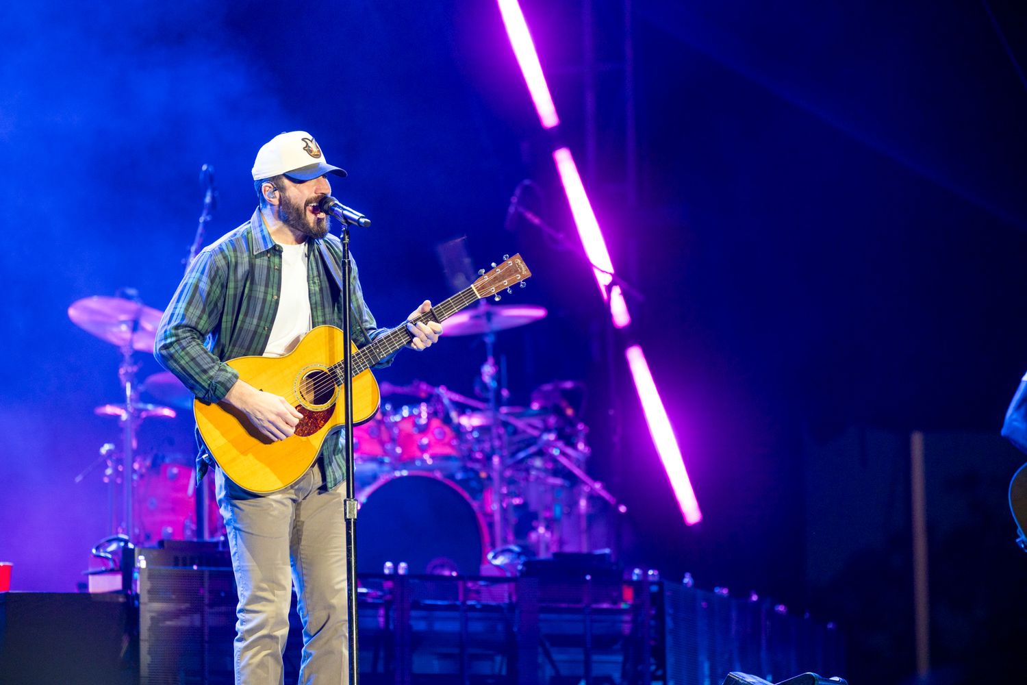 Country music performer plays acoustic guitar on stage with bright purple lighting and concert production setup.
