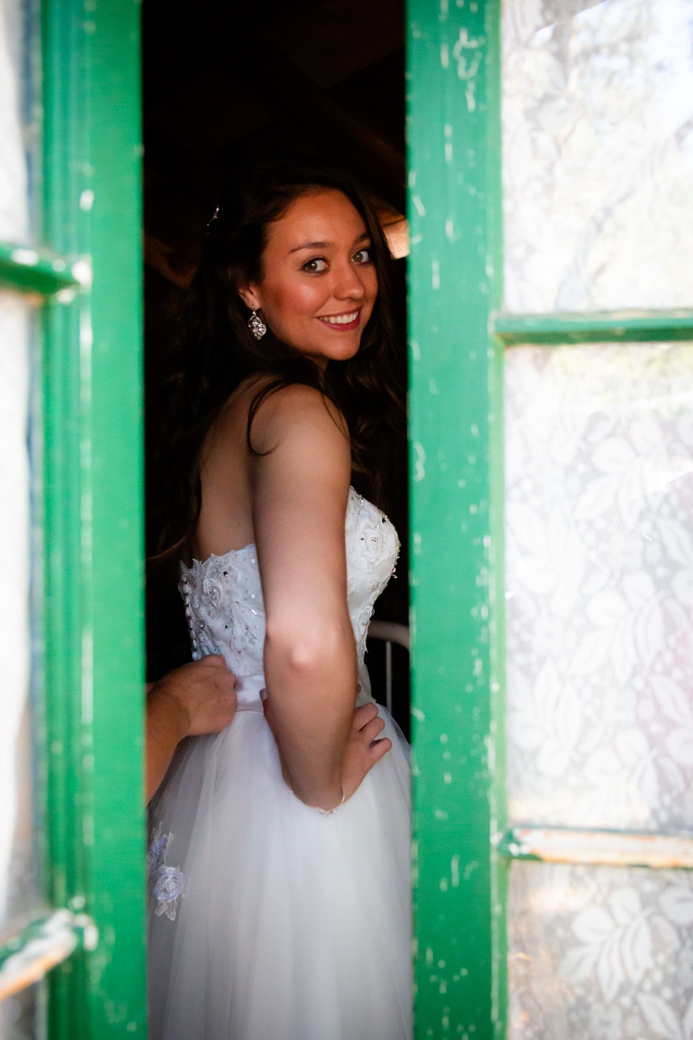A wedding dress is beautifully framed by a rustic green doorway in natural lighting.