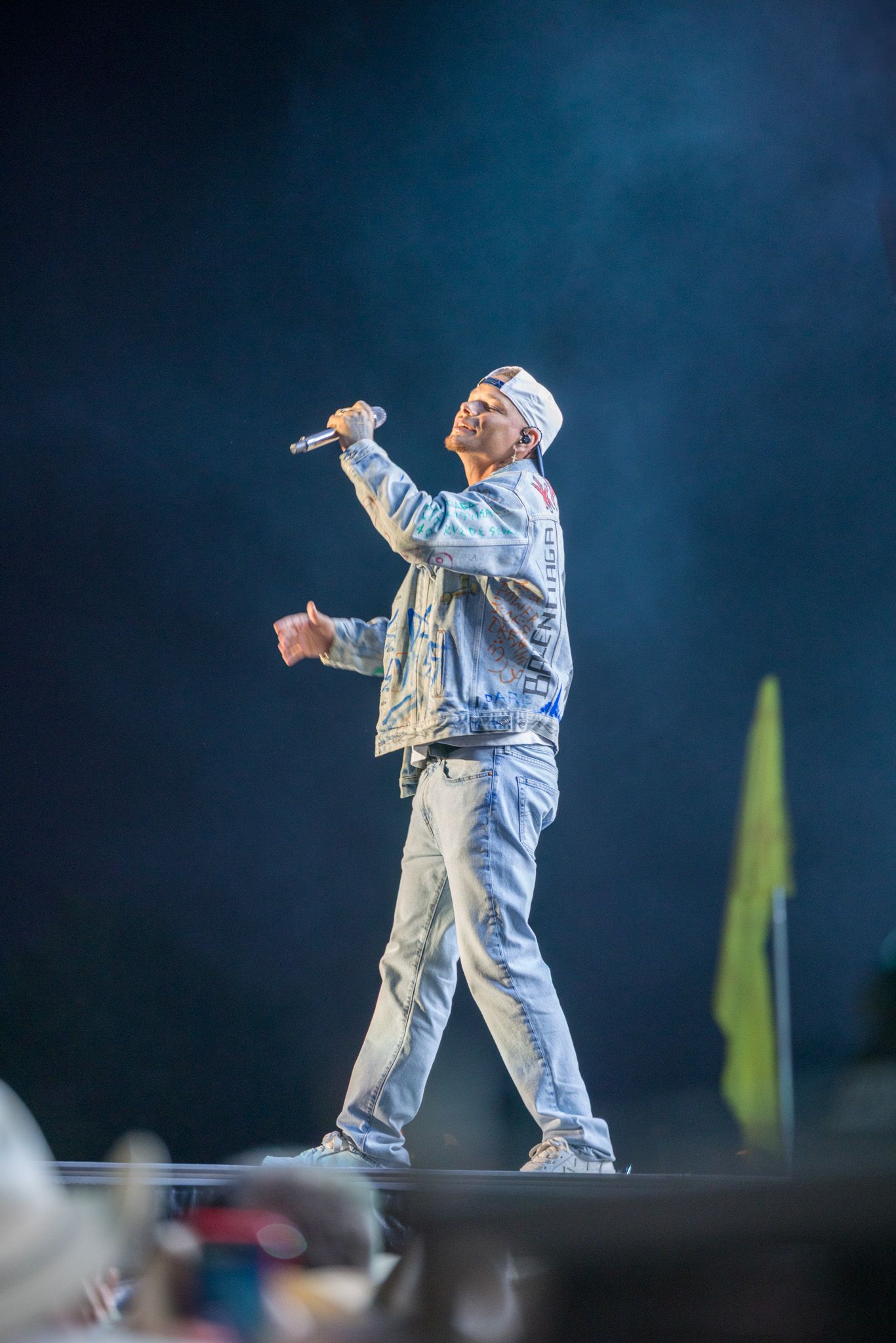 Performer in white outfit performs on stage against deep blue backdrop during live concert.