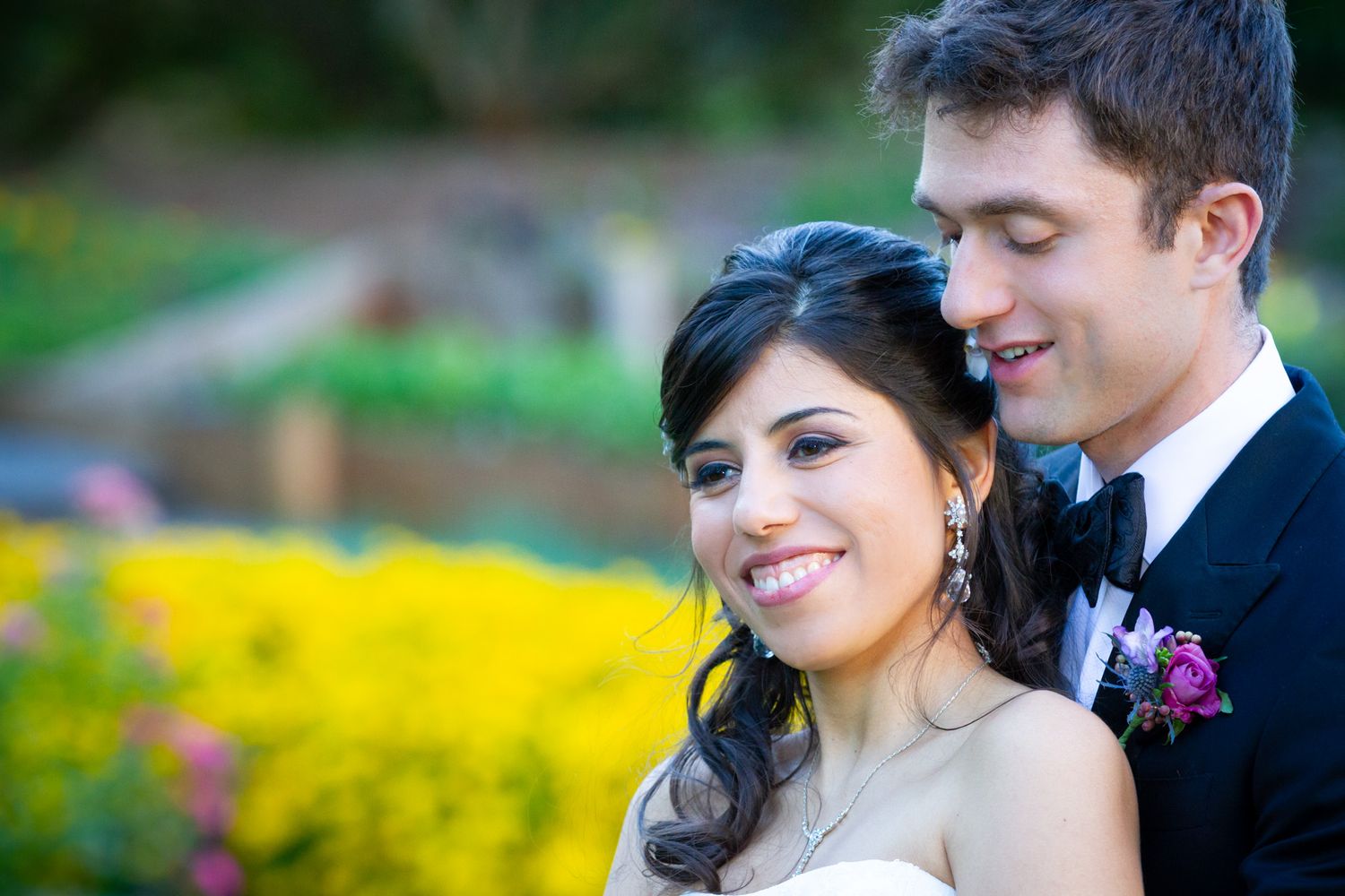 Elegant wedding couple posing together in a garden with vibrant yellow flowers in the background.