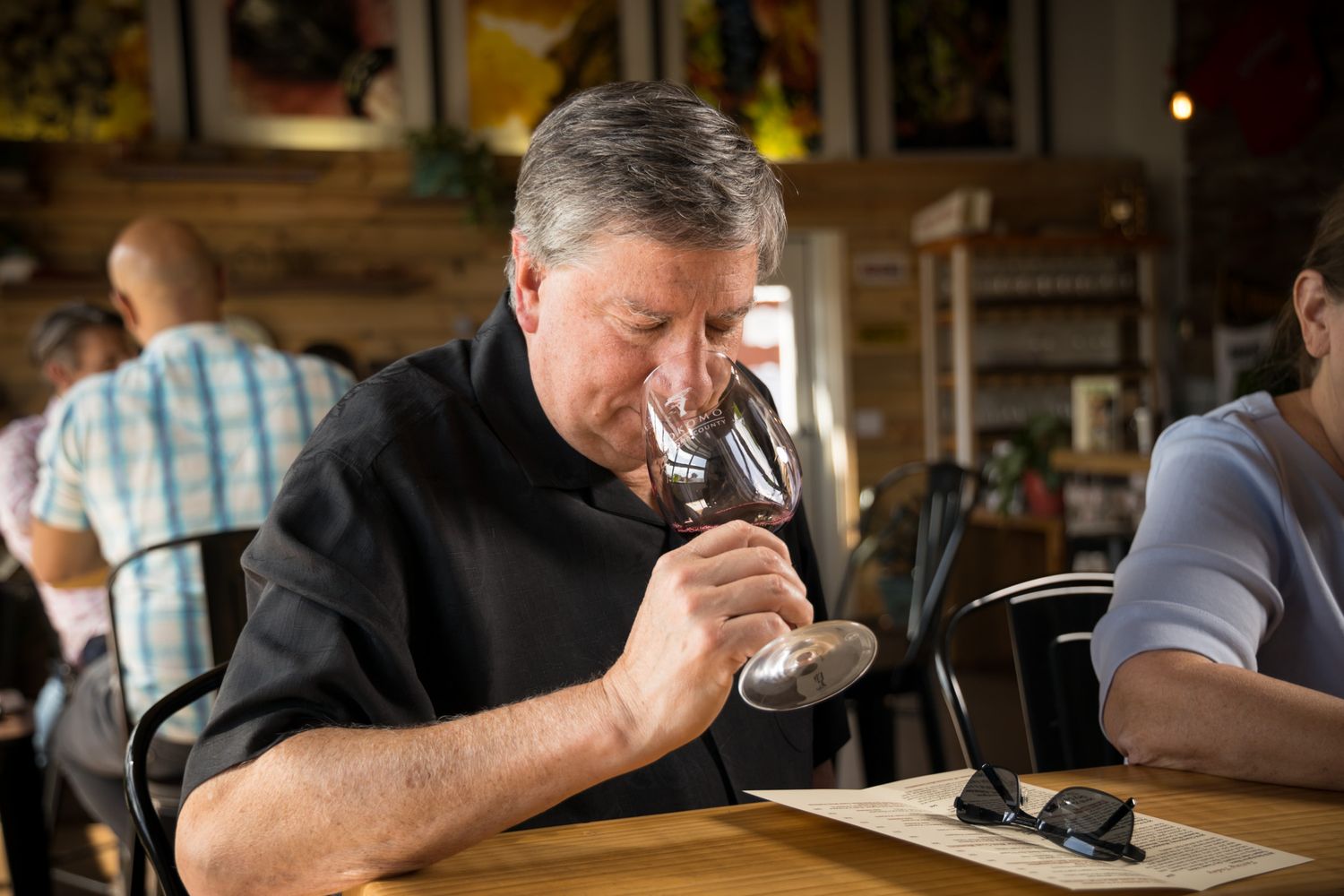 Person smelling wine from glass at rustic restaurant table.
