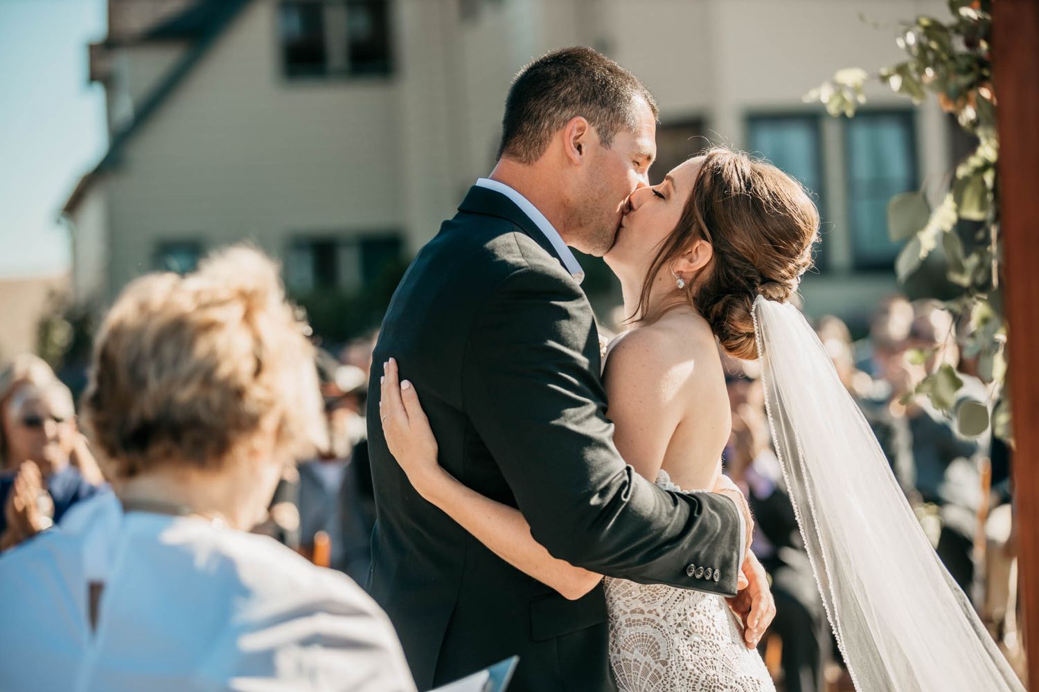 Romantic outdoor wedding ceremony kiss in front of white house.