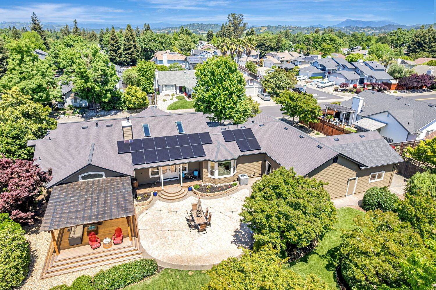 Aerial view of modern suburban home with solar panels on roof surrounded by lush greenery.