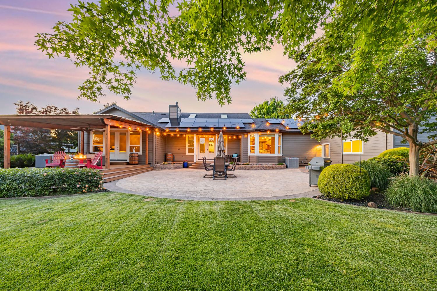Beautiful backyard with stone patio and landscaping at dusk with warm lighting.