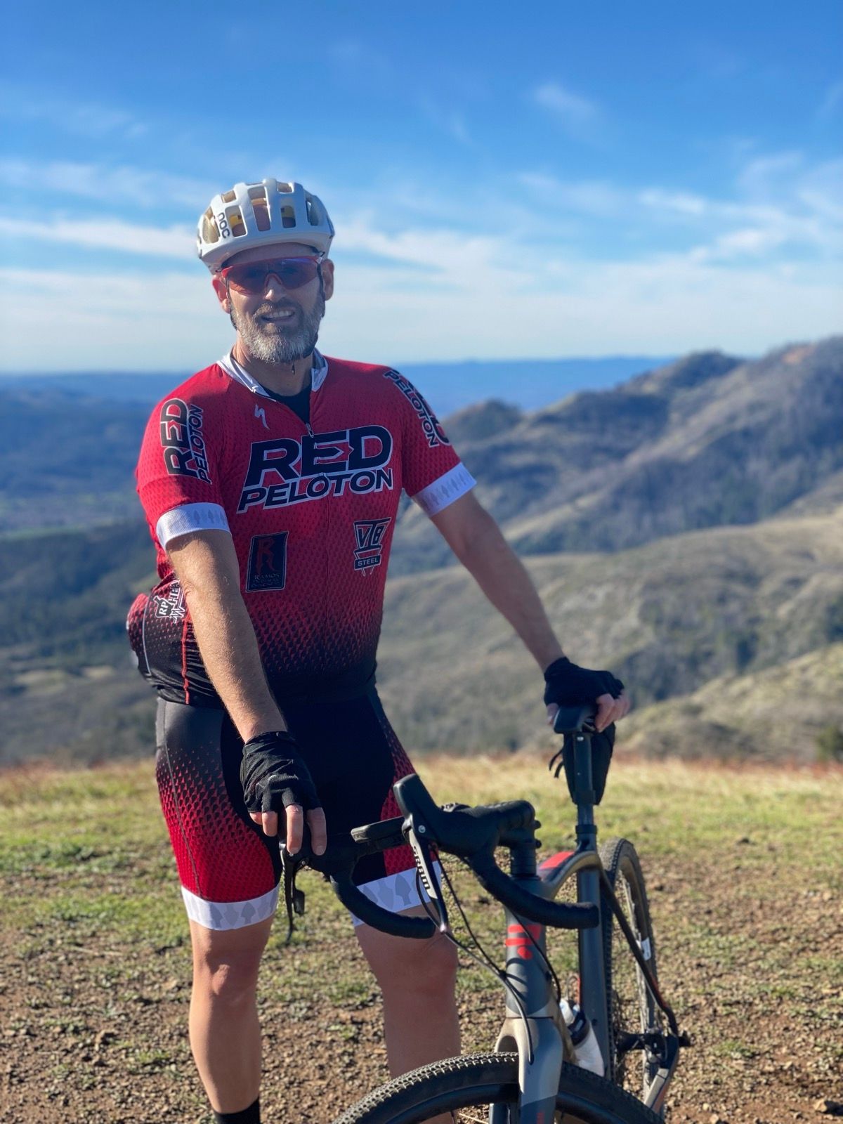 Cyclist in red jersey with mountain bike poses on scenic mountain overlook.