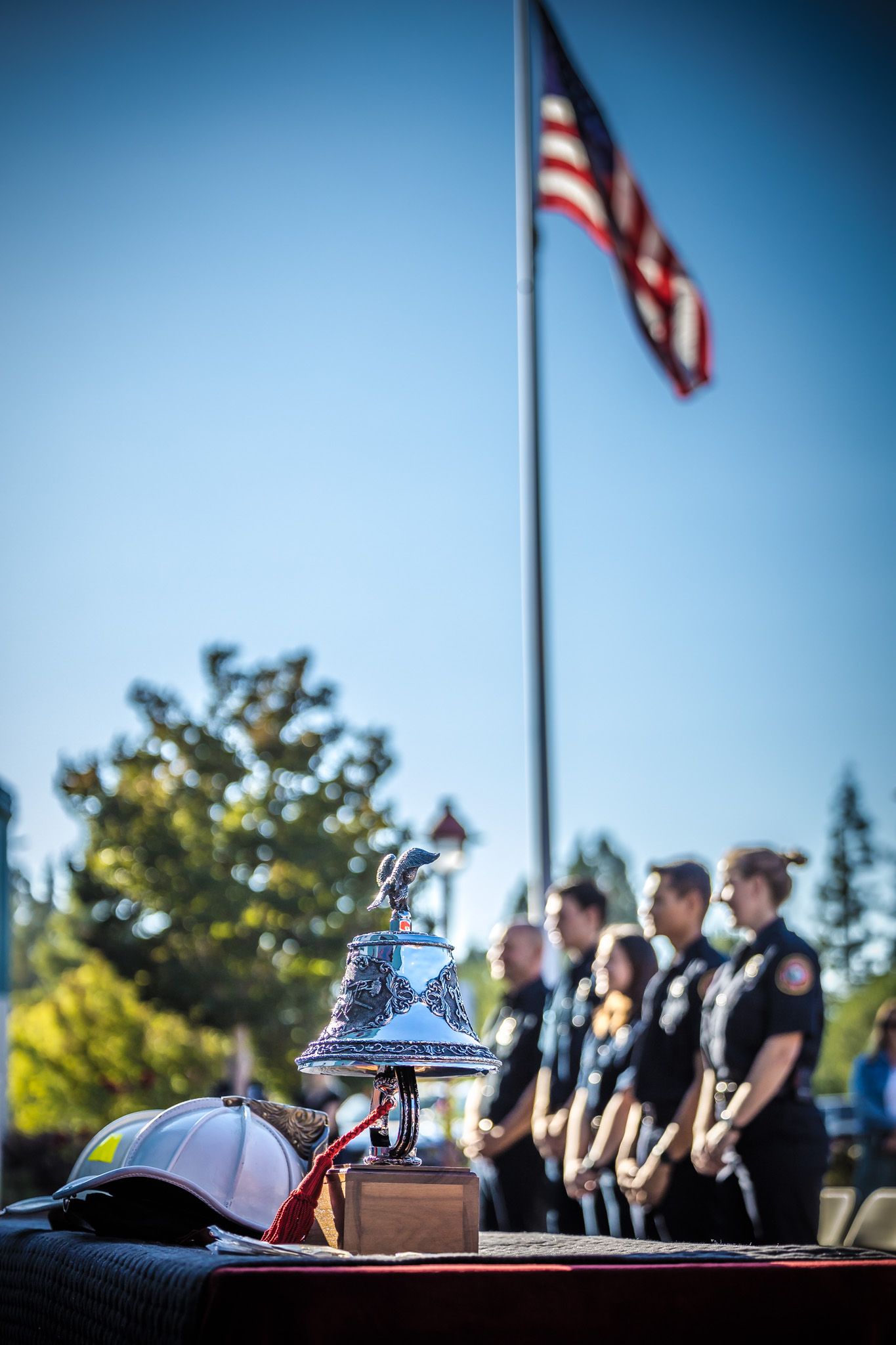 A ceremonial bell displayed with an American flag and honor guard in the background.