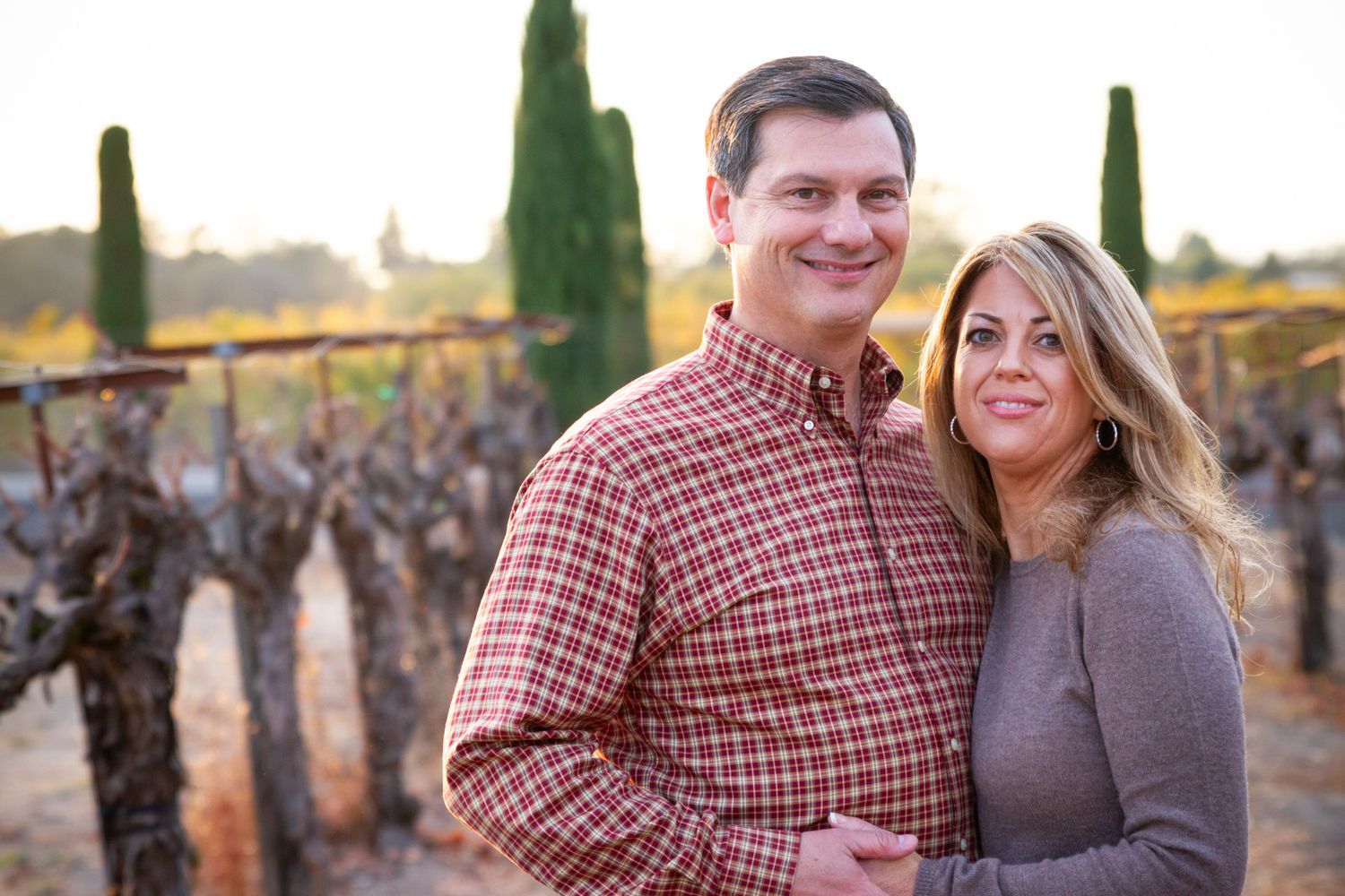 Couple poses together in vineyard setting during golden hour.