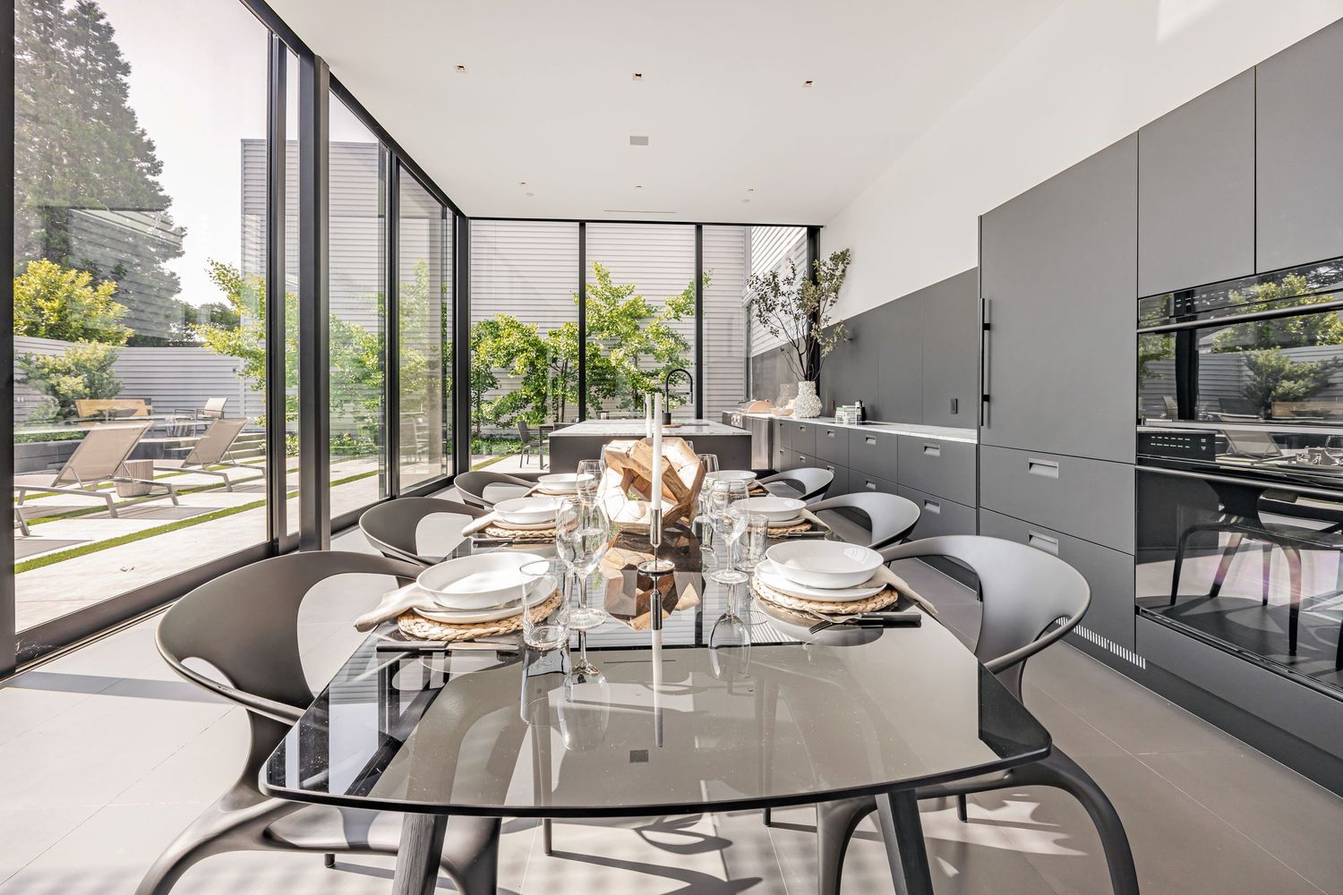 Modern open concept kitchen with white marble countertops and floor-to-ceiling windows overlooking an outdoor space.