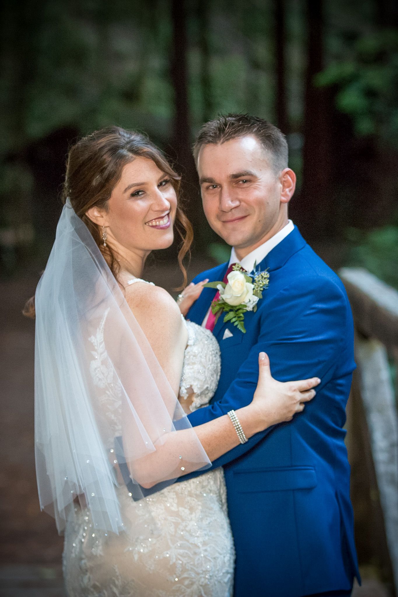 Joyful wedding couple sharing loving moment in forest setting with elegant attire.