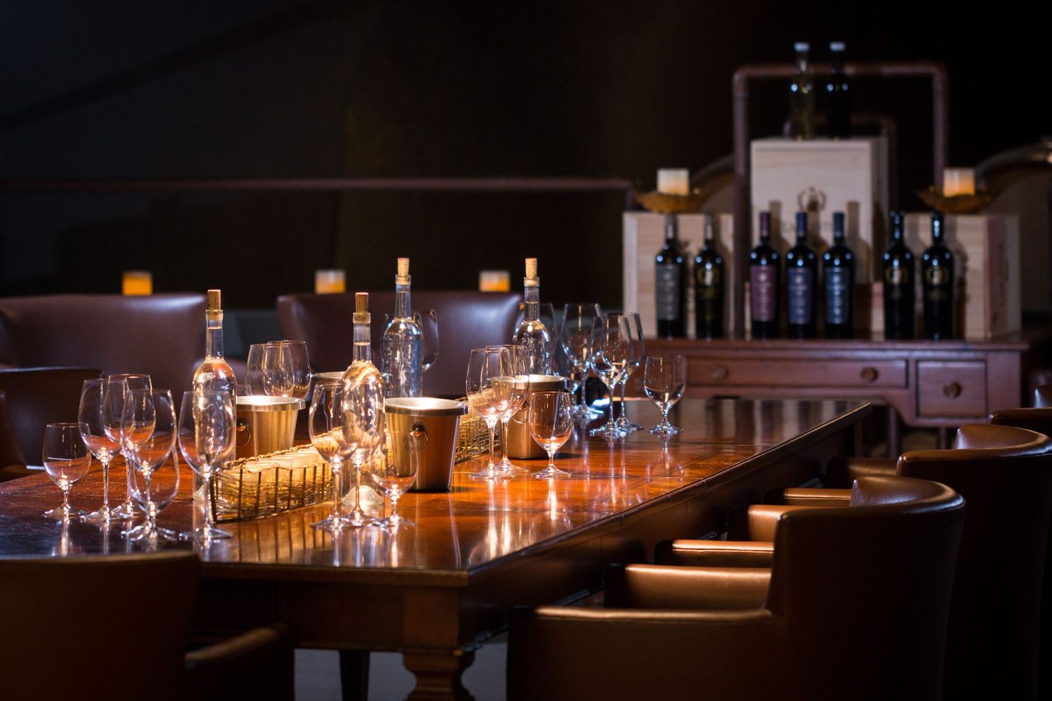 Elegant wine bar setup with empty glasses and bottles on wooden table in dim lighting.