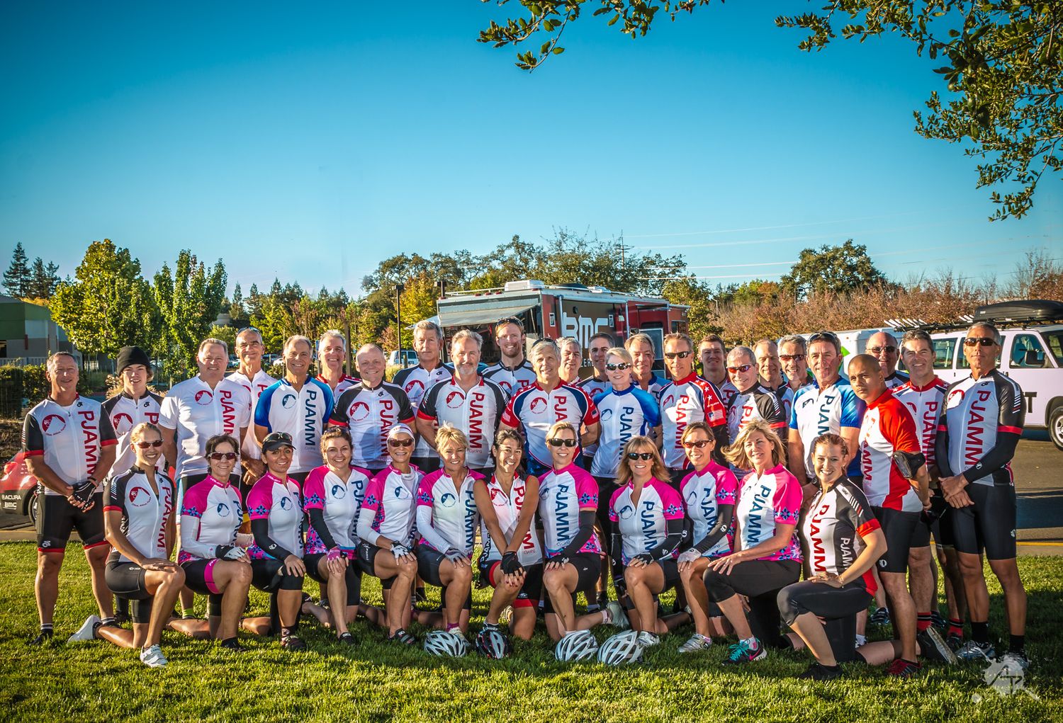 Large group of rugby players in matching purple and white jerseys pose together for a team photo on sunny grass field.