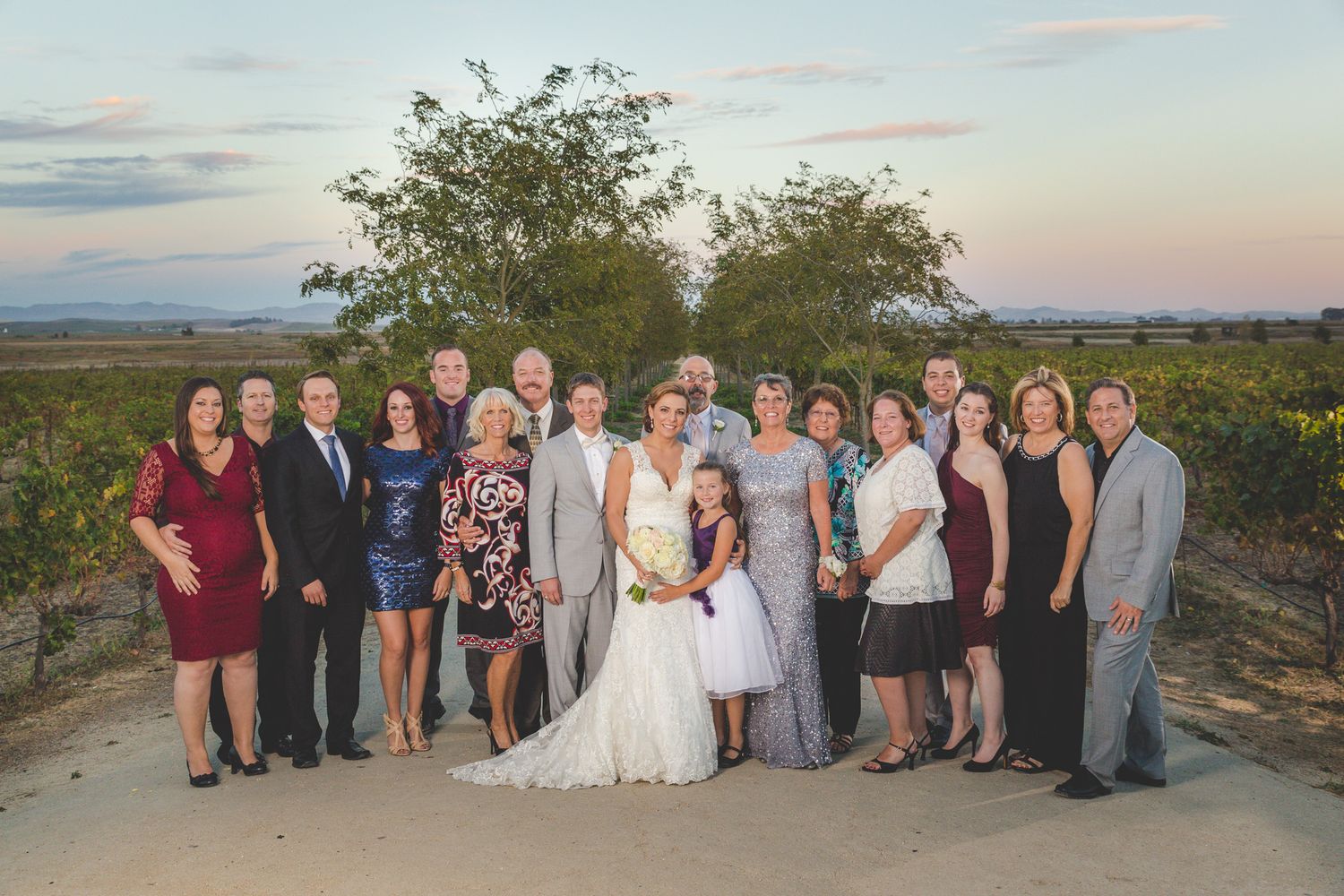Wedding party poses outdoors at sunset in a vineyard with mountains in the distance.