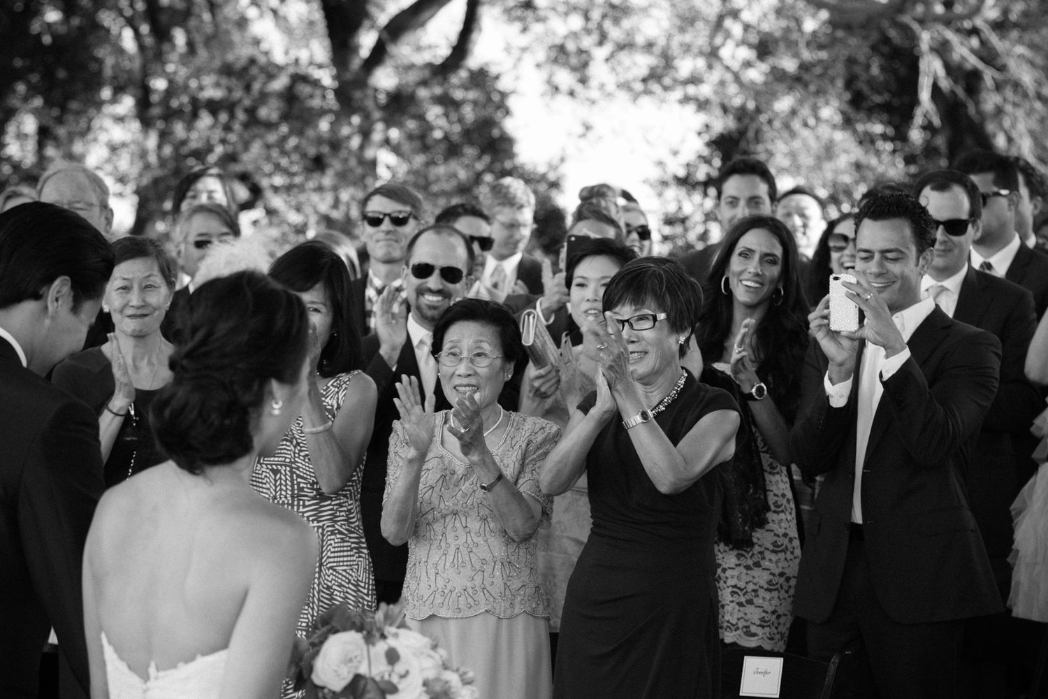 Black and white photo of wedding guests enthusiastically applauding during ceremony.