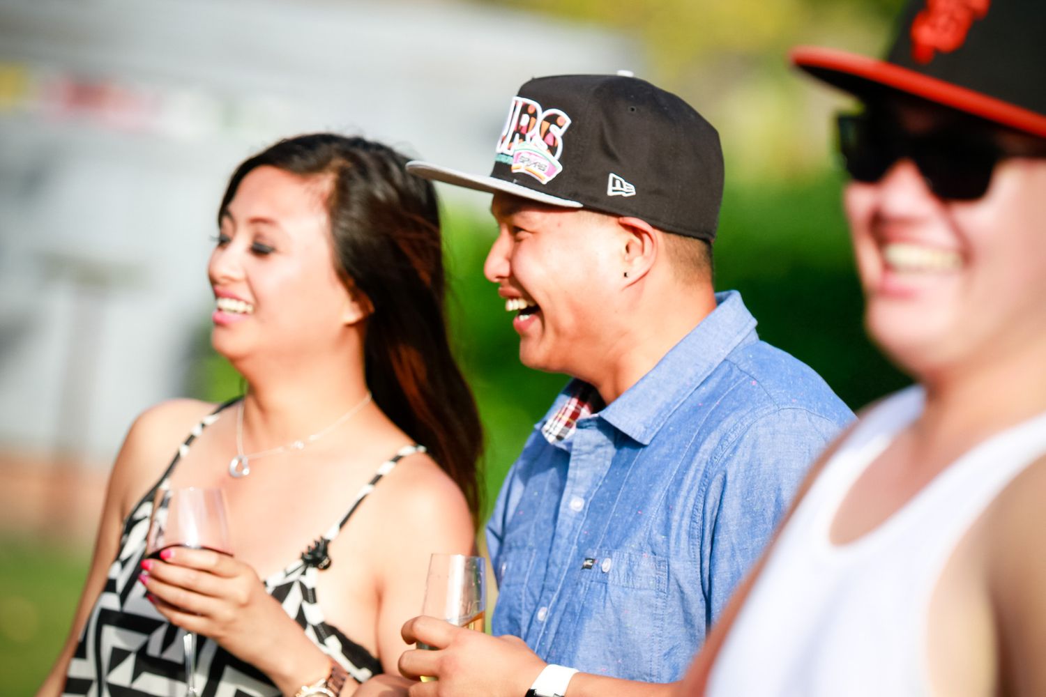 Three friends enjoying an outdoor event with one wearing a baseball cap and sunglasses.