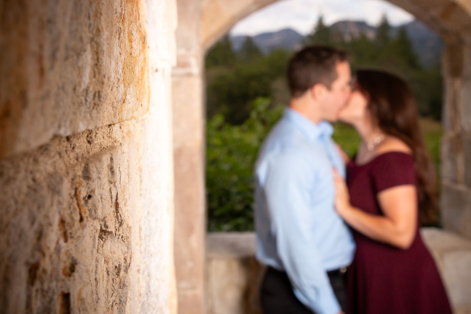 Soft focus shot of couple kissing in stone archway with natural backdrop.