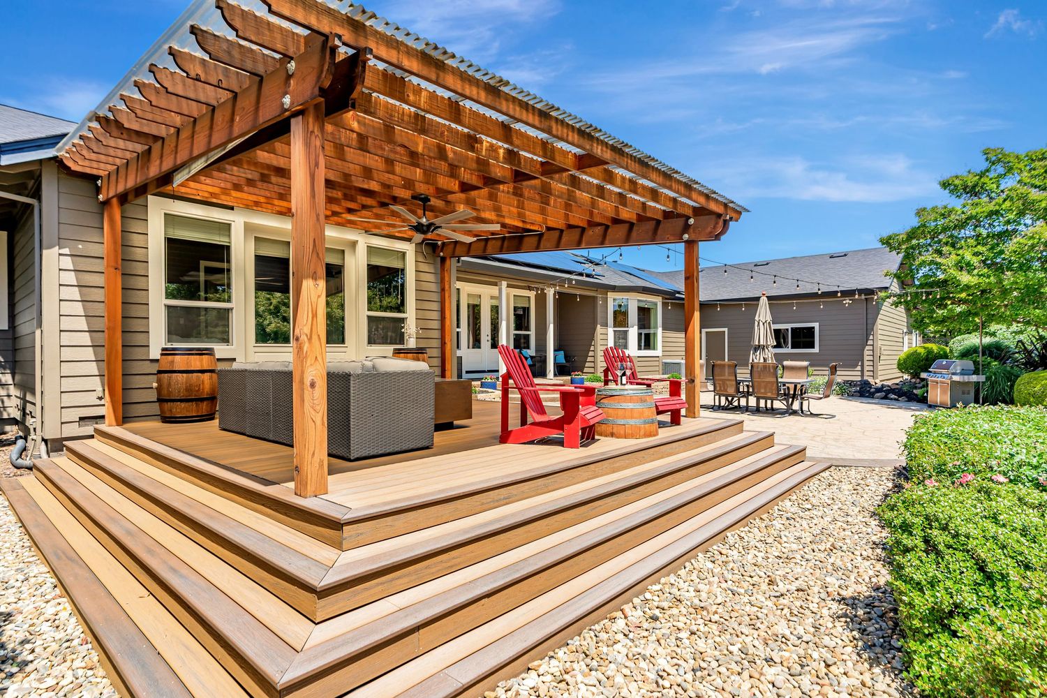 Elevated deck with wooden pergola featuring tiered steps and red outdoor furniture.