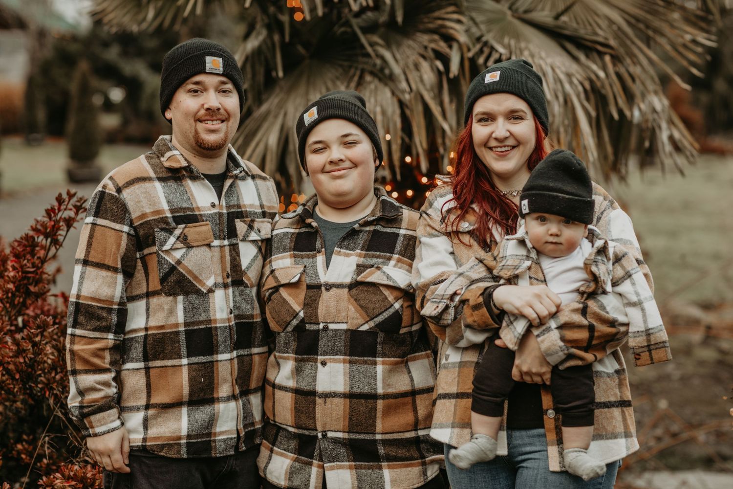 Family wearing coordinated brown and white plaid flannel shirts poses together outdoors in autumn setting.