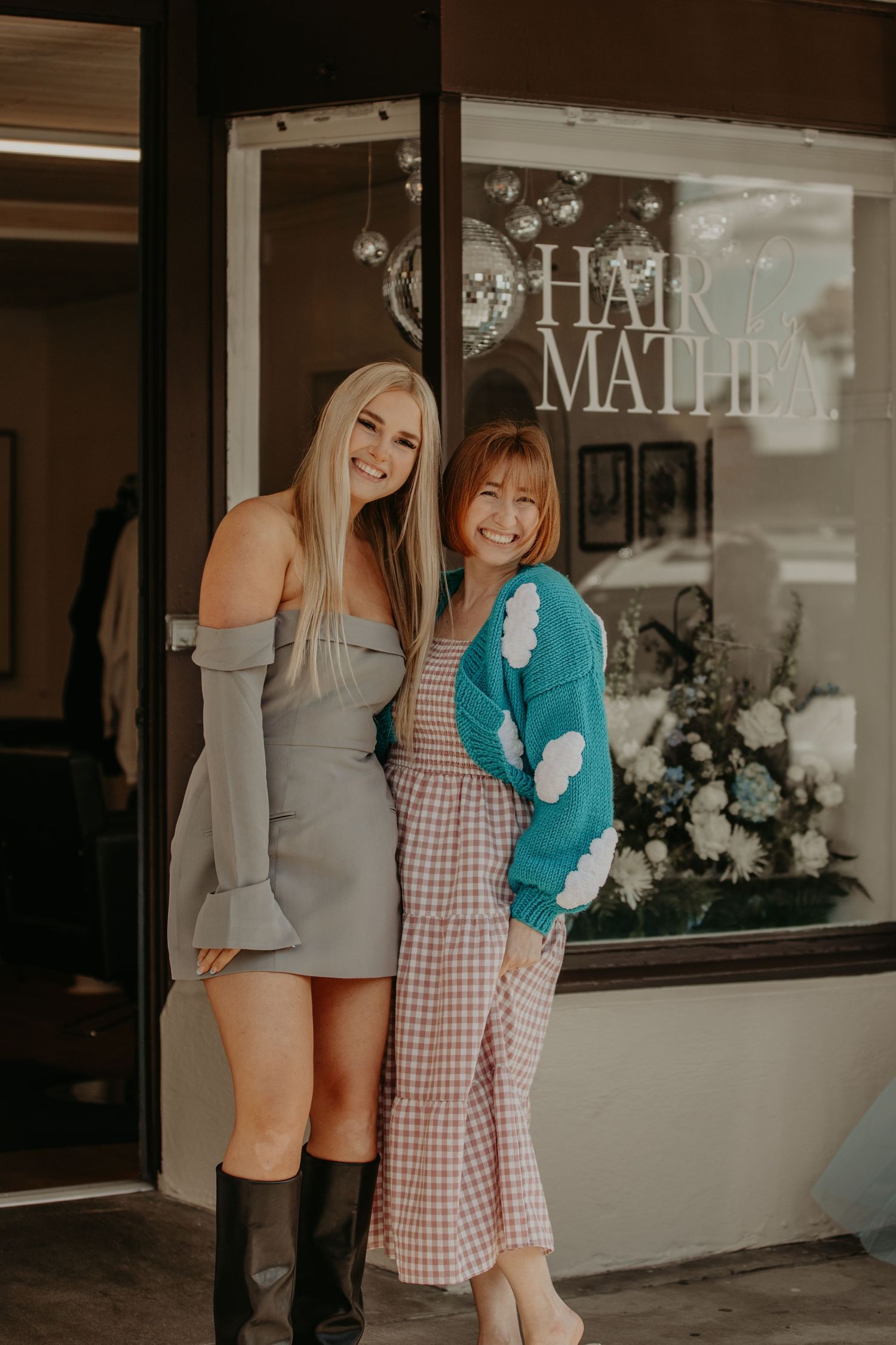 Two people stand smiling outside a storefront window with 'Hair Matlie' signage and floral decorations.