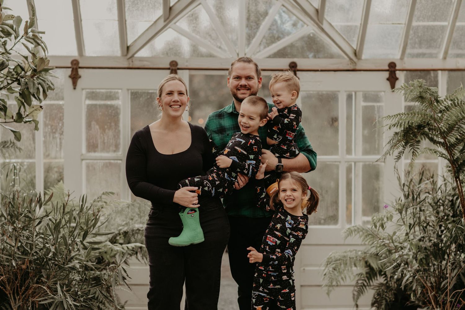 A family poses together inside a bright greenhouse with plants and natural lighting.