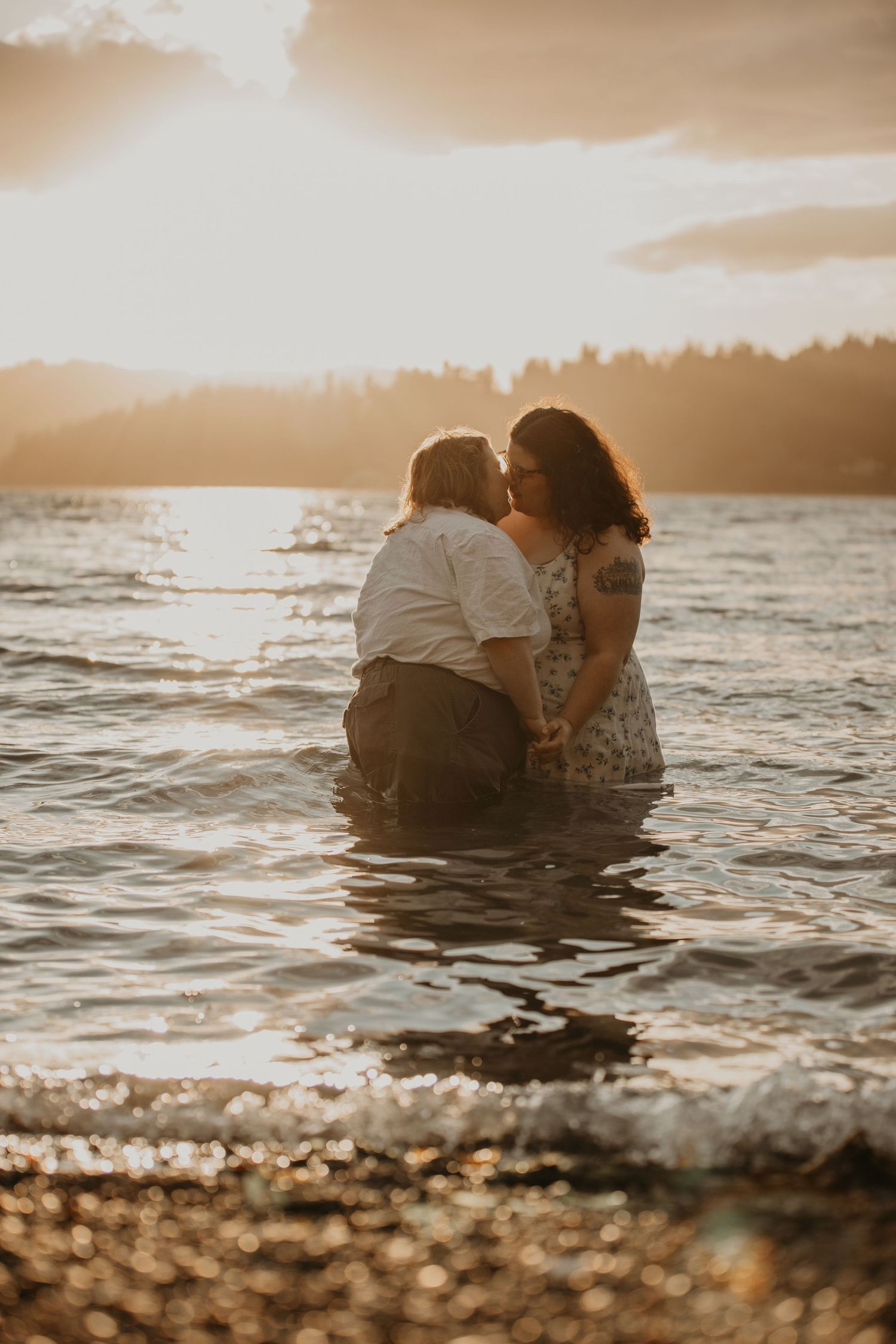 Two people share an intimate moment while wading in ocean waters during a golden sunset.