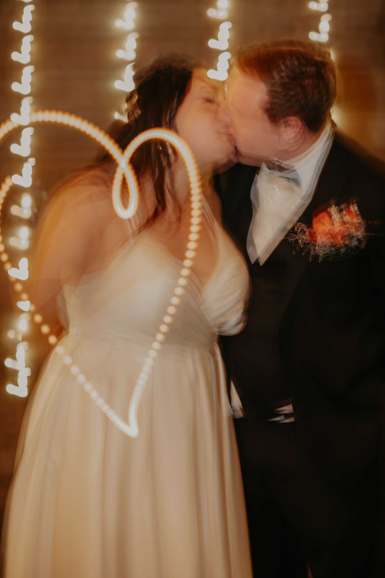 A romantic moment between newlyweds kissing under twinkling fairy lights at their wedding reception.