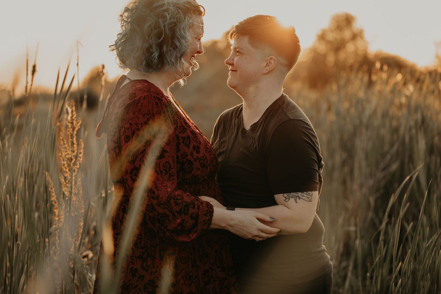 A couple embraces in a golden sunlit field with tall grass during sunset creating a romantic silhouette.