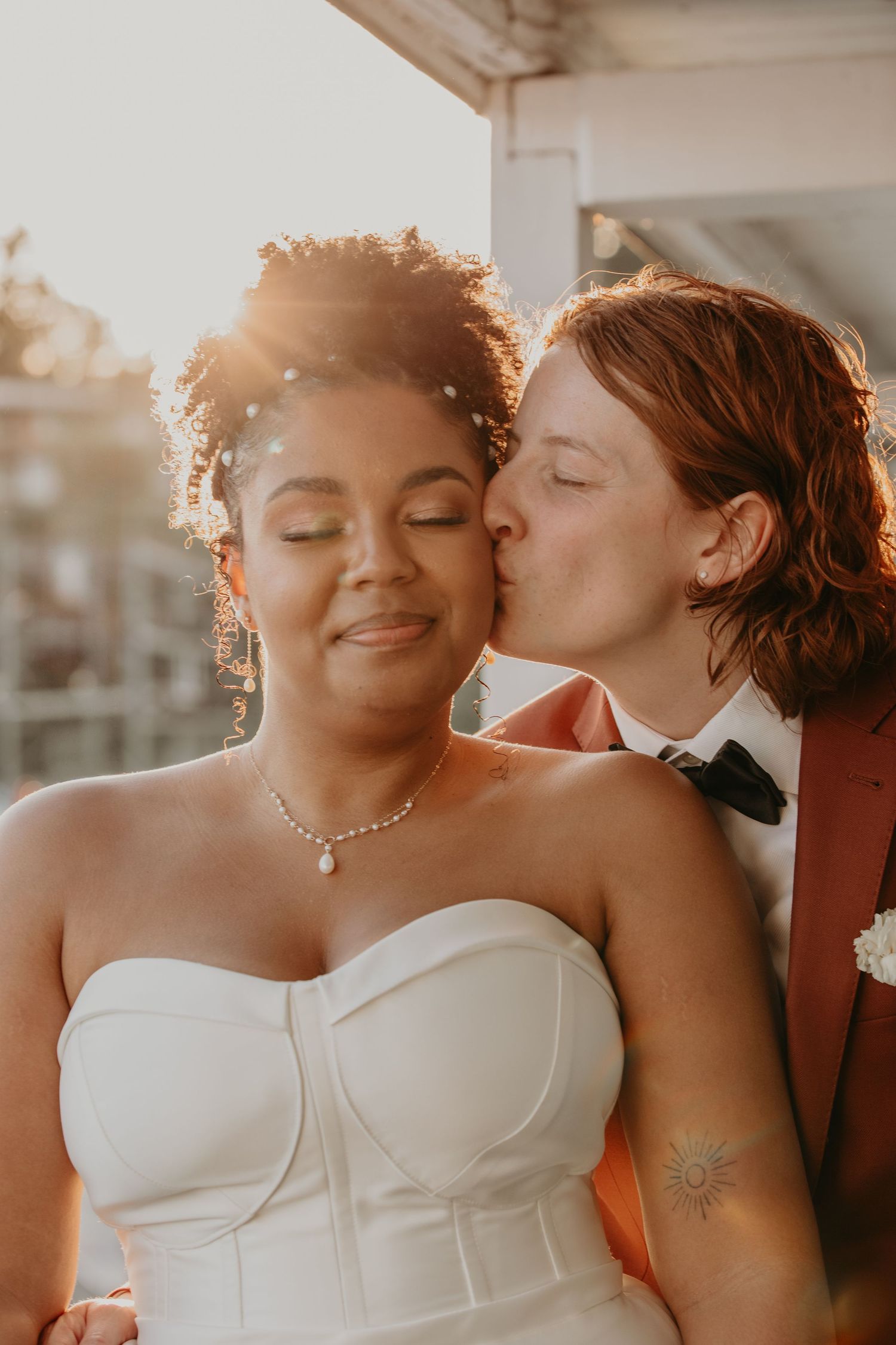 An intimate golden hour wedding portrait on a rooftop with one person in white and one in rust-colored attire.