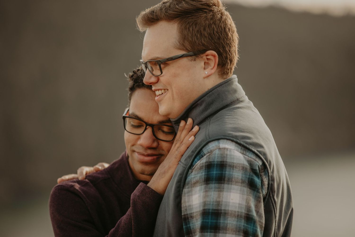 A tender moment between two people embracing outdoors at sunset while wearing cozy plaid and sweaters.