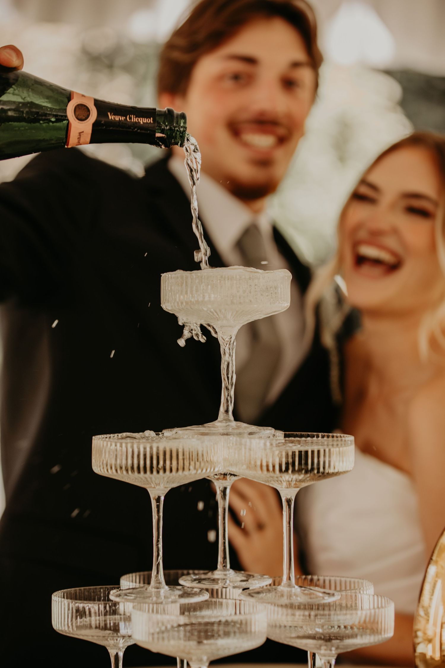 Champagne being poured into a vintage-style coupe glass tower at a wedding celebration.