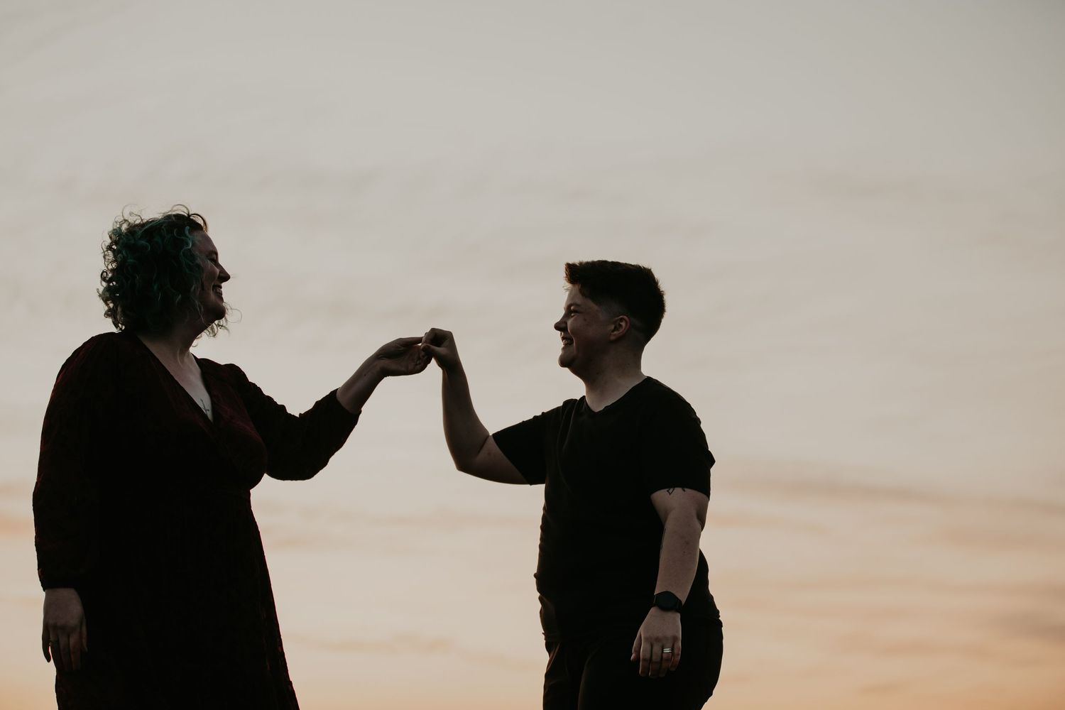 Silhouetted figures joining hands against warm sunset sky.