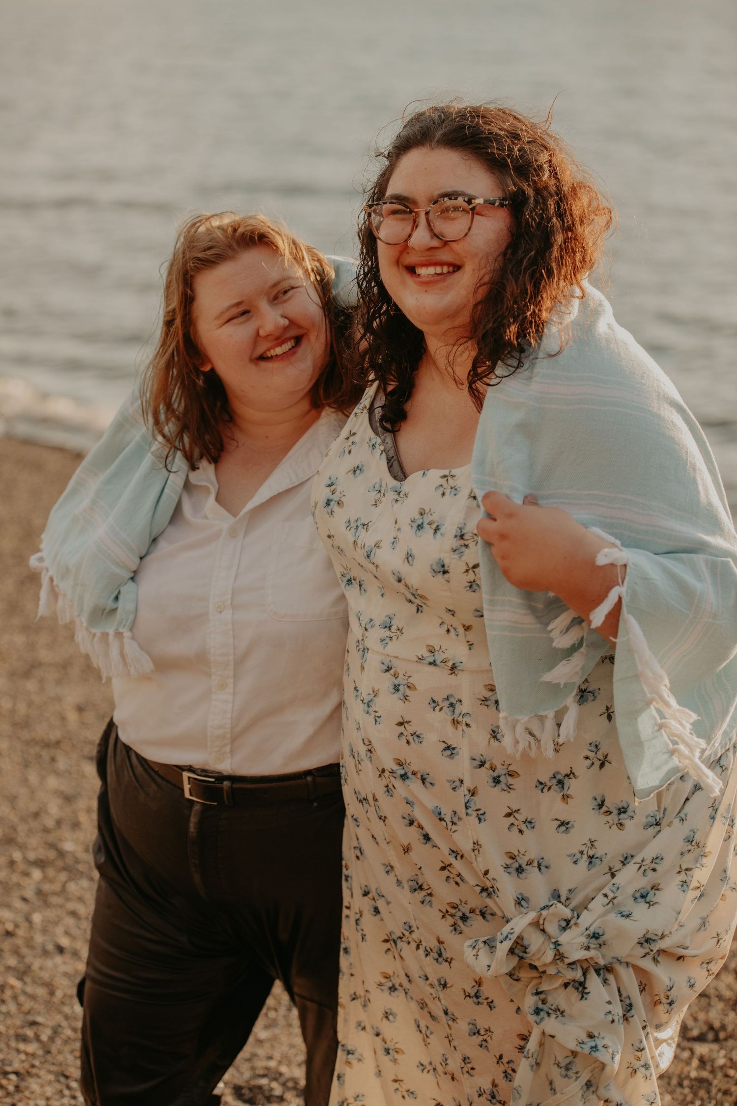 Two people embracing and laughing together on a beach during golden hour.