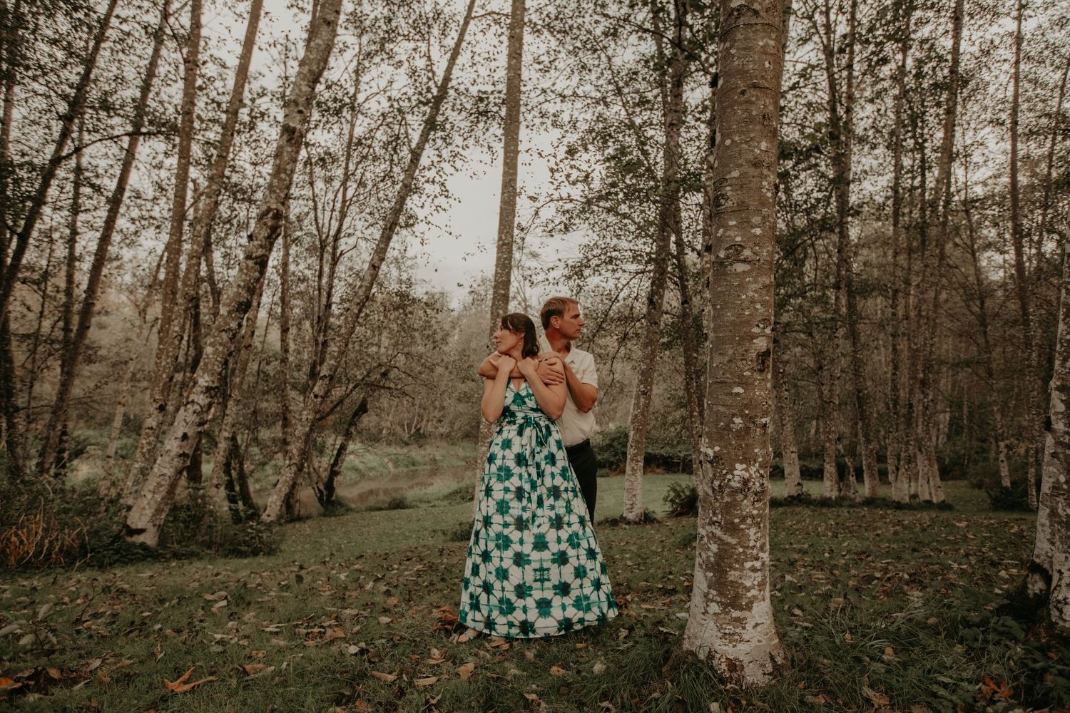 A couple embraces in a romantic moment among tall birch trees while wearing a polka dot dress.