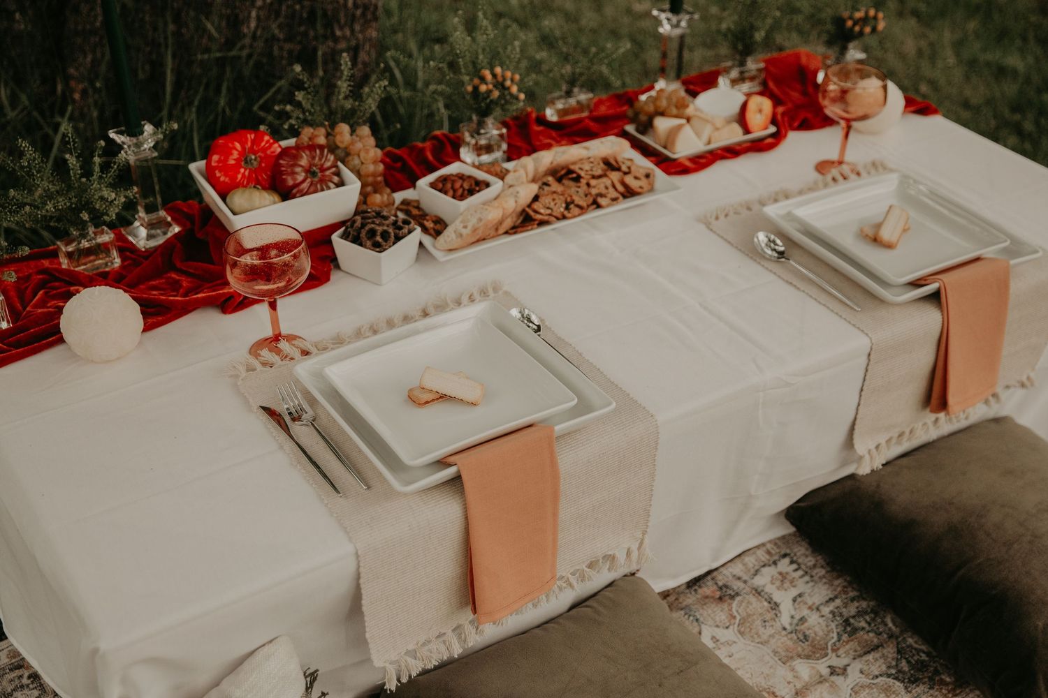 Wedding reception table set with white linens, square plates, and red accents for an elegant outdoor celebration.