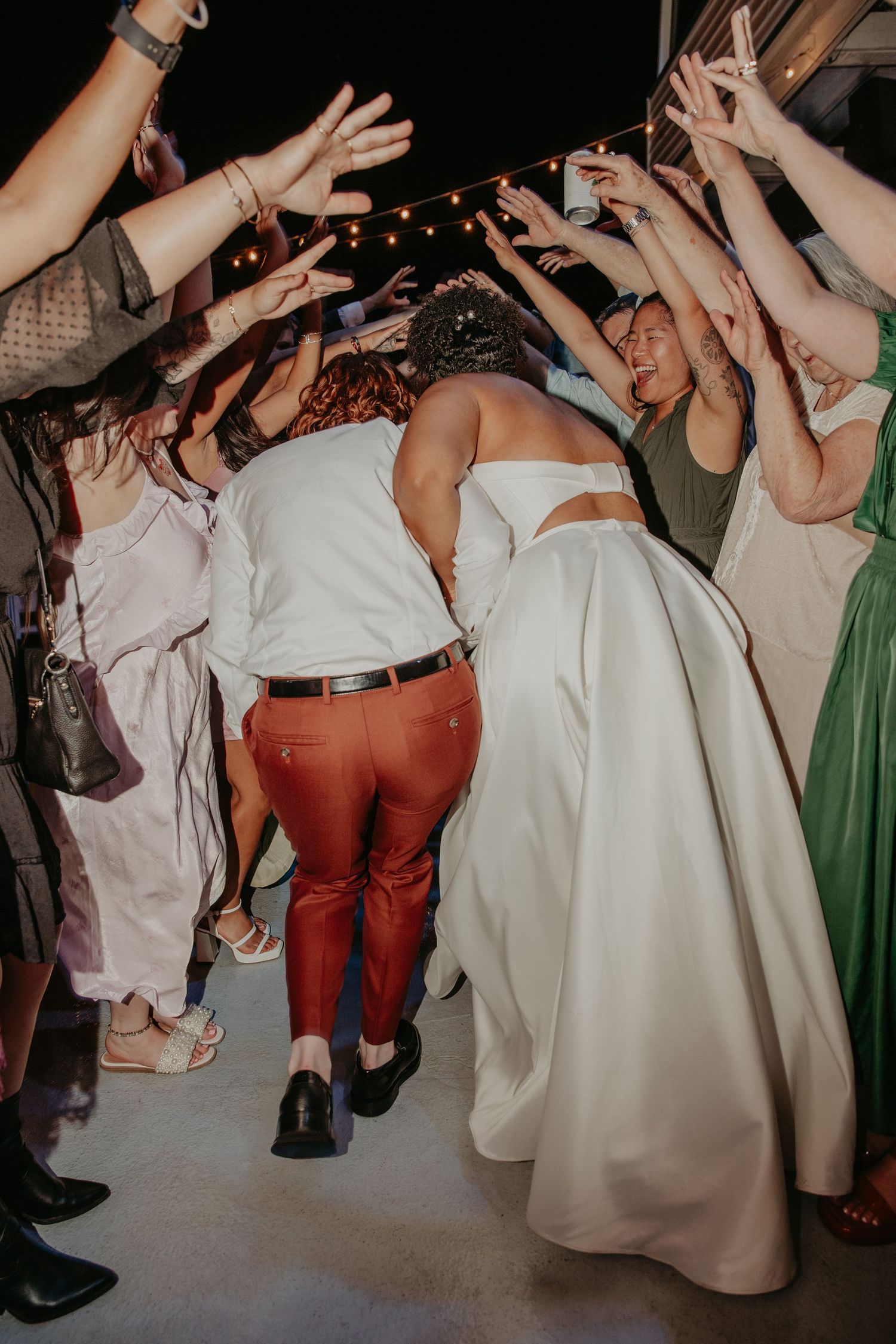 Dance floor filled with celebration and movement at a wedding reception showing white dresses and red pants.