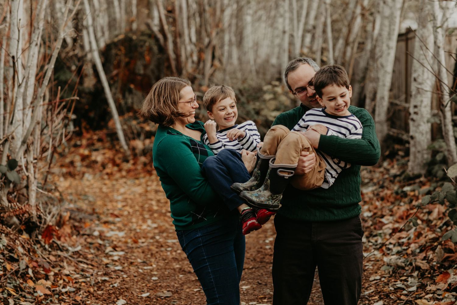 An outdoor autumn photo of people in green sweaters spending time together in a wooded area.