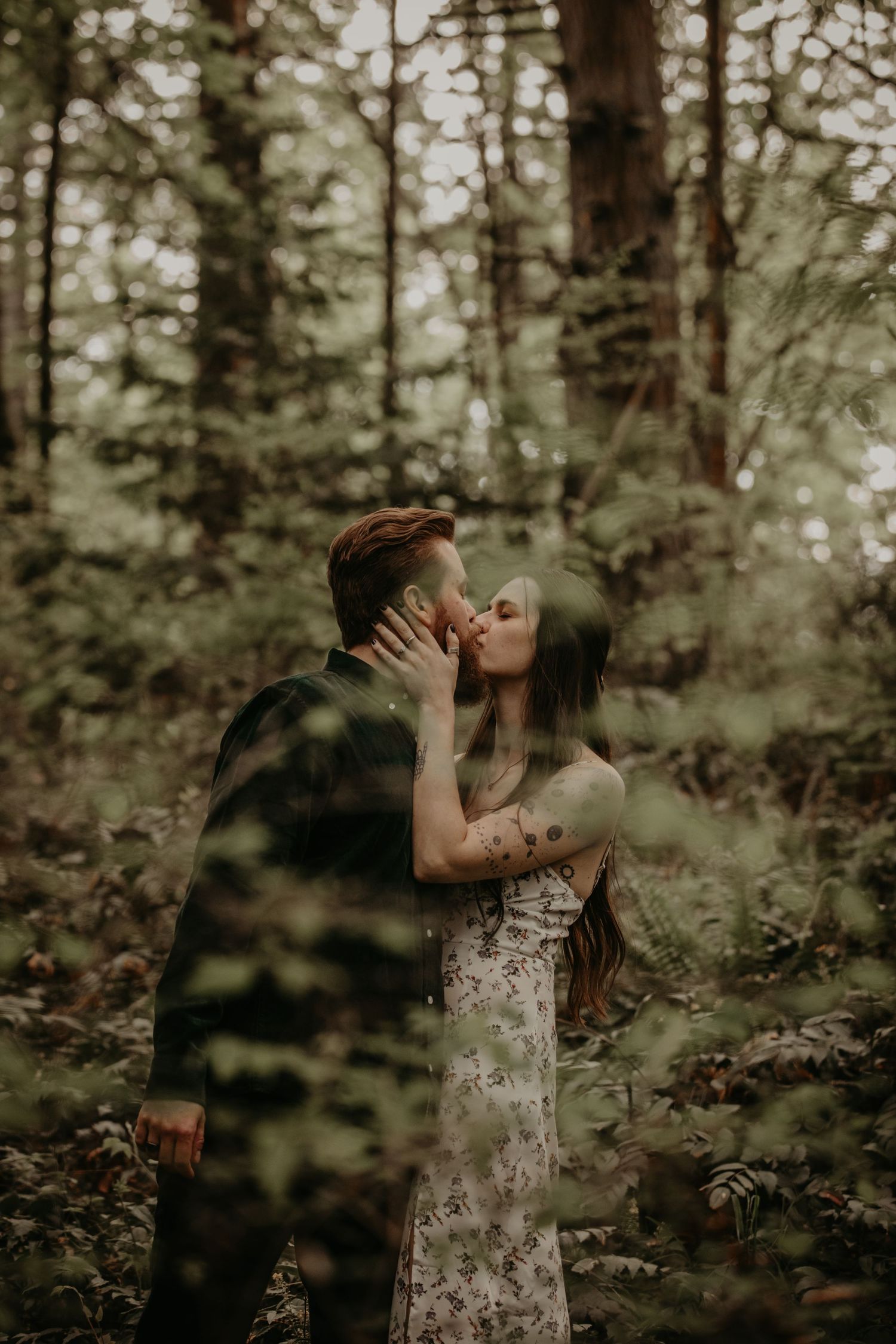 A romantic embrace shared between a couple in a moody forest setting with soft lighting filtering through the trees.